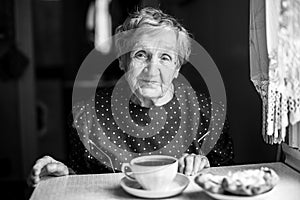 Elderly woman drinking tea in the kitchen.