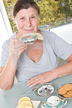 Elderly woman drinking tea with lemon and biscuits.