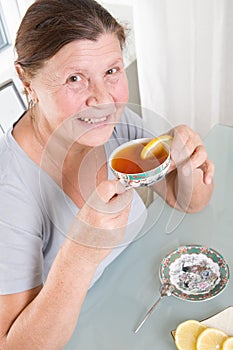 Elderly woman drinking tea with lemon and biscuits.