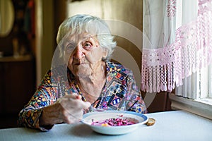 An elderly woman eating soup sitting at a table.