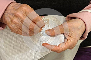 An elderly woman is embroidering a cross-stitch picture, hands close-up