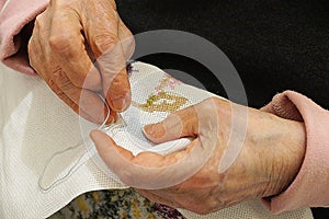 An elderly woman is embroidering a cross-stitch picture, hands close-up