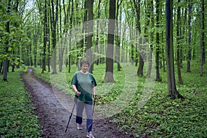 elderly woman is engaged in Nordic walking with sticks in the spring forest