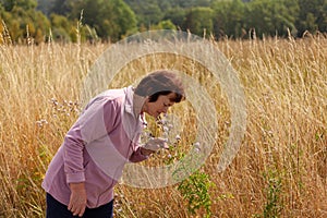 Elderly woman enjoying the beauty and fragrance of wildflowers in a tranquil wheat field setting