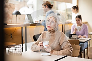 Elderly woman enjoying cup of coffee in cozy cafe