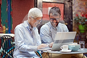An elderly woman enjoying a laptop content while spending free time with her young male friend at bar`s garden. Leisure, bar,