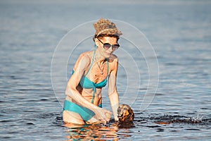 Elderly woman enjoying outdoor activities playing ball in river swimming with her cute dog Dachshund breed. concept pets, love for