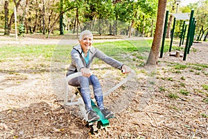 Elderly Woman Exercising At Outdoor Fitness Park With Rowing Machine