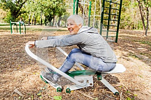 Elderly Woman Exercising At Outdoor Fitness Park With Rowing Machine