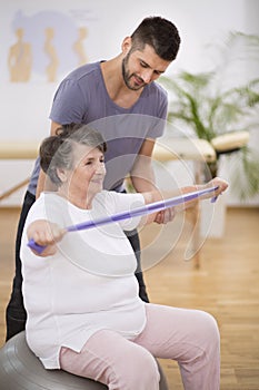 Elderly woman exercising with stretching tapes with her physiotherapist