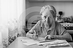 Elderly woman fills out utility bills sitting in the kitchen.