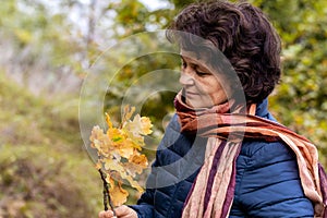 Elderly woman in the forest admires the autumn leaves, a woman holds an oak branch with yellow leaves