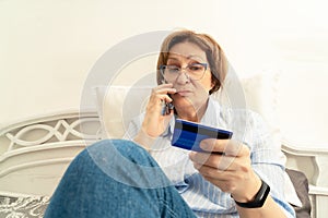 Elderly woman frustratedly talking on a mobile phone and holding a bank card in her hand