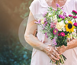 Elderly woman get a beautiful bouquet of field flowers. Senior lady holding a bunch of flowers.