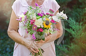 Elderly woman get a beautiful bouquet of field flowers. Senior lady holding a bunch of flowers.