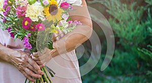 Elderly woman get a beautiful bouquet of field flowers. Senior lady holding a bunch of flowers.