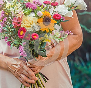 Elderly woman get a beautiful bouquet of field flowers. Senior lady holding a bunch of flowers.