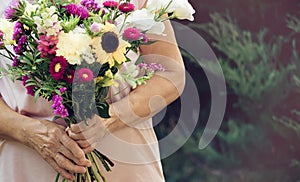 Elderly woman get a beautiful bouquet of field flowers. Senior lady holding a bunch of flowers.