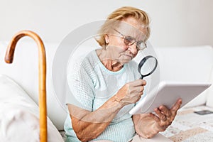 Elderly woman with glasses and loupe using a digital tablet