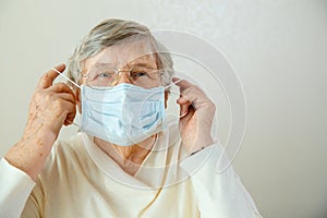 An elderly woman in glasses puts on a medical mask on her face