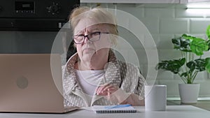Elderly woman in glasses is upset that she can't do something on laptop computer