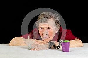 An elderly woman with gray hair looks longingly at the glassware. The woman`s hand is chained to a plastic Cup as a concept of