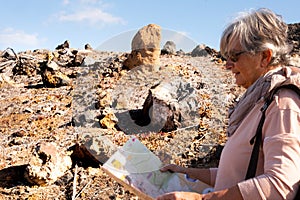 Elderly woman gray hair relax during an excursion to check the map. enjoy the nature hiking in a desert place with volcanic rocks