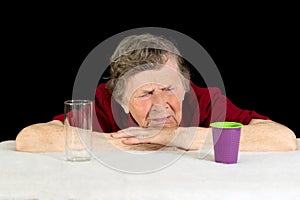 An elderly woman with gray hair and wrinkles on her face looks at the disposable plastic Cup with disgust and contempt. The