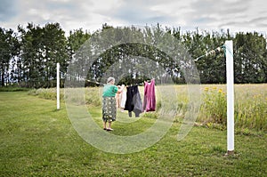 Elderly woman hanging clothes on the line outside.