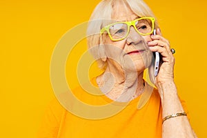 elderly woman happy lifestyle in yellow t-shirts with phone yellow background