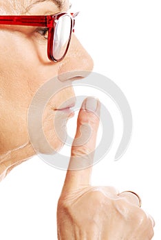Elderly woman is having finger on her lips. Profile.
