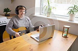 An elderly woman in headphones takes guitar lessons online. A retired senior woman studying online, watching music