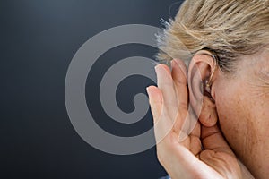 Elderly woman with hearing aid on grey background. Deafness concept.