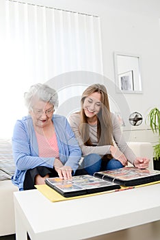 Elderly woman with her young granddaughter at home looking at memory in family photo album