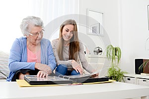 Elderly woman with her young granddaughter at home looking at memory in family photo album