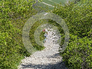 An elderly woman is hiking uphill along a rocky path.