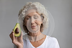 Elderly woman hold fresh avocado recommending natural cosmetics