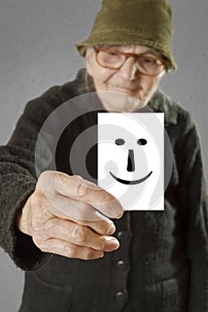 Elderly woman holding card with printed happy emoticon.