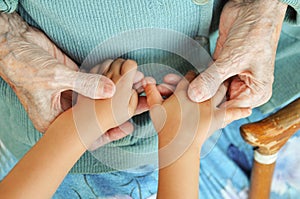 An elderly woman holding children`s hands, a wooden cane on the street. great-grandmother and great-grandson