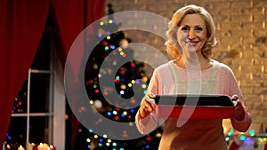 Elderly woman holding Christmas dish looking into camera, holiday atmosphere