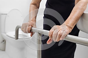 Elderly woman holding on handrail in toilet.