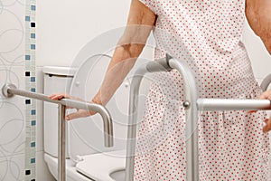 Elderly woman holding on handrail in toilet.