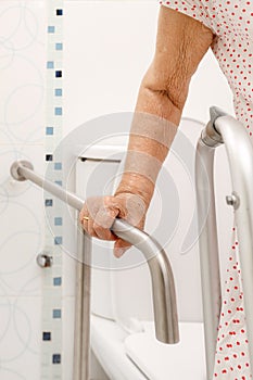 Elderly woman holding on handrail in toilet.