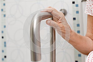 Elderly woman holding on handrail in toilet.