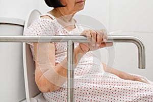 Elderly woman holding on handrail in toilet.