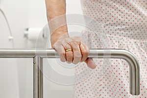 Elderly woman holding on handrail in toilet.