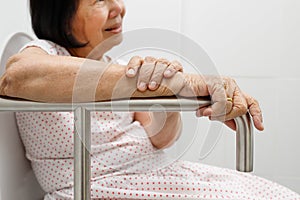 Elderly woman holding on handrail in toilet.