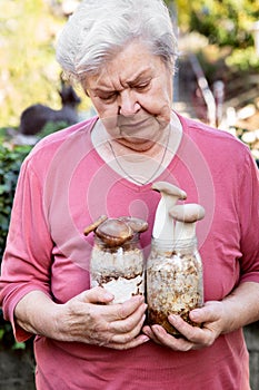 Elderly woman holding home cultivated mushrooms, selfmade fungiculture on glasses