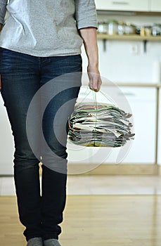 Elderly woman holding old magazines for recycling at home