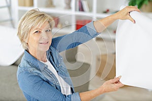 elderly woman holding paint roller for wallpaper